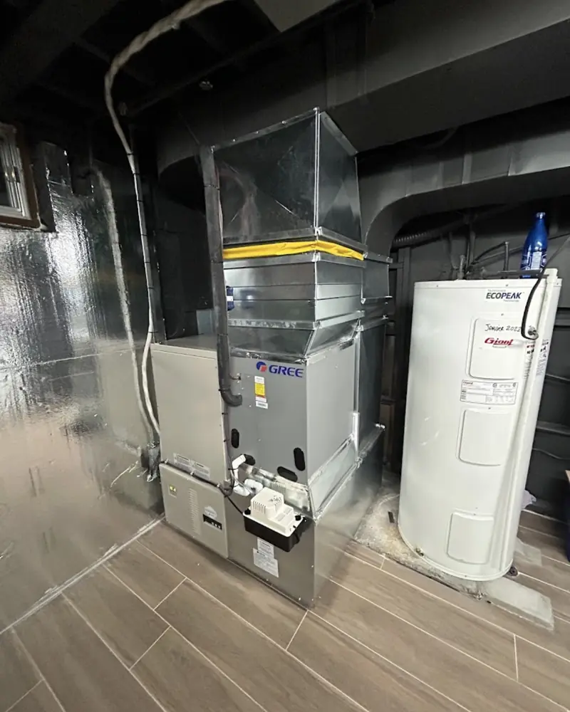 Thermopompe centrale Gree installée dans un sous-sol fini, à côté du chauffe-eau