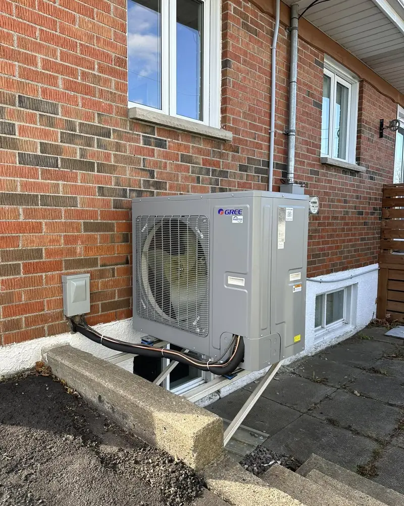 Condenseur de thermopompe Gree installé sur support contre une maison en brique