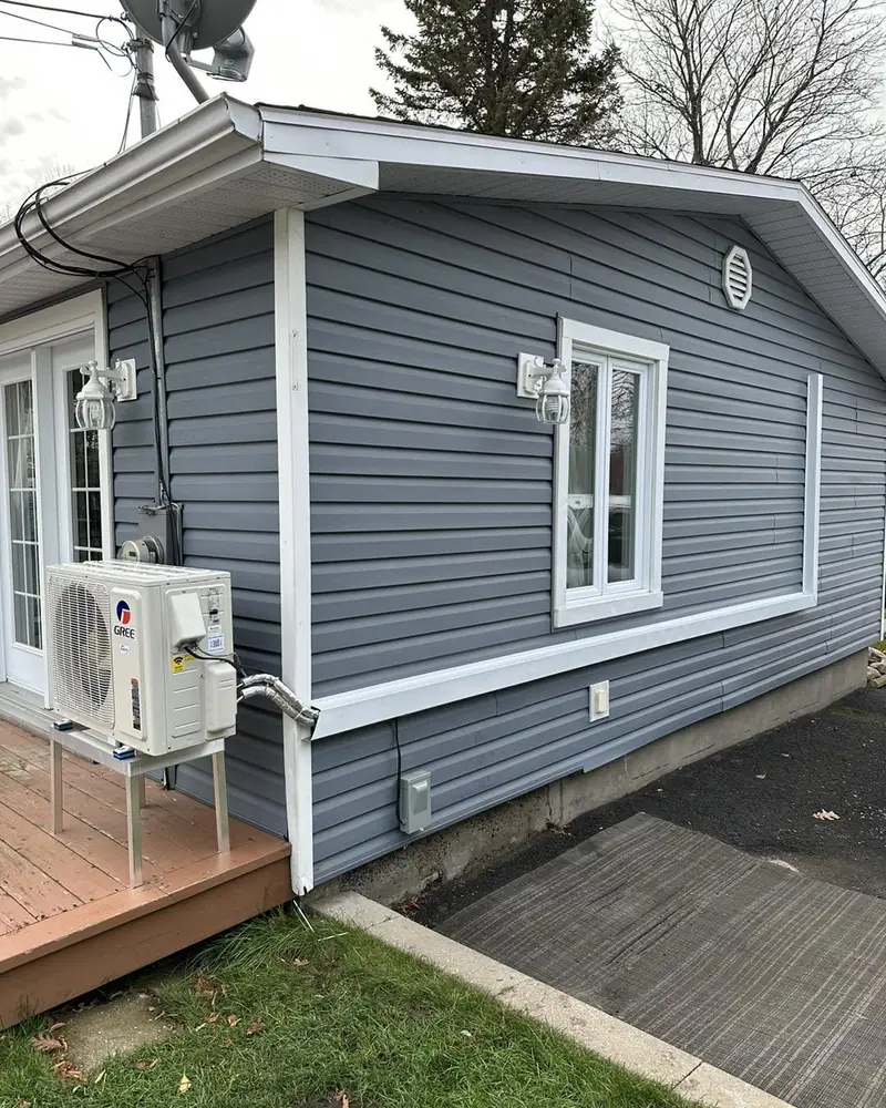 Condenseur de thermopompe murale Gree installé sur une galerie, maison au revêtement gris