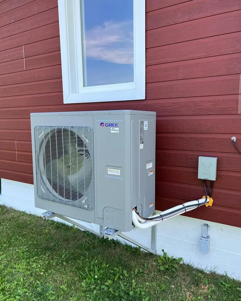 Condenseur de thermopompe centrale Gree sur support, devant une maison au revêtement rouge