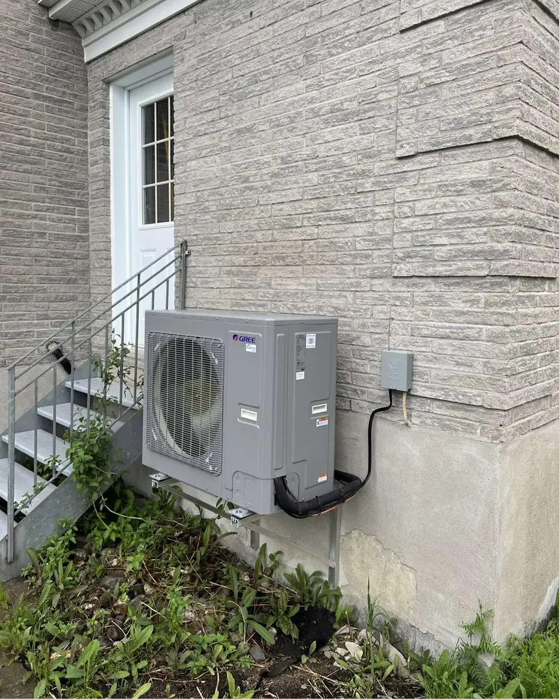 Condenseur de thermopompe Gree sur support mural, à côté d'un escalier extérieur, maison en pierre